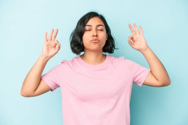 Mavi arka planda izole edilmiş genç Latin kadın yoğun bir günün ardından rahatlıyor, yoga yapıyor..