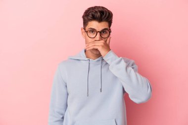 Pembe arka planda izole edilmiş genç beyaz adam elleri endişeli bir şekilde ağzı örtüyor..