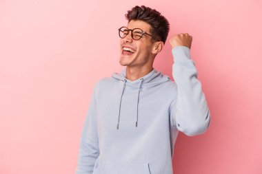 Pembe arka planda izole edilmiş genç beyaz bir adam zaferi, tutkuyu ve coşkuyu kutluyor, mutlu bir ifade..