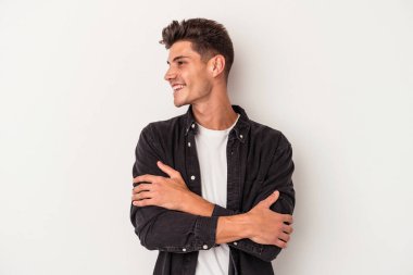 Beyaz arka planda izole edilmiş genç beyaz adam kollarını kavuşturarak gülümsüyor..
