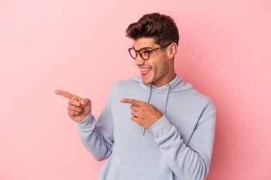 Kafkasyalı genç adam pembe arka planda izole edilmiş, başparmak uzakta, gülüyor ve kaygısız..