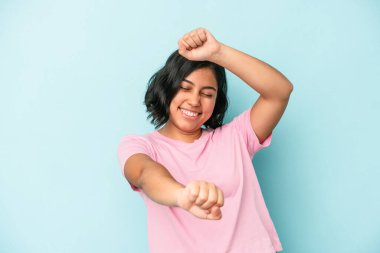 Mavi arka planda izole edilmiş genç Latin kadın özel bir günü kutluyor, atlıyor ve enerjiyle kollarını kaldırıyor..