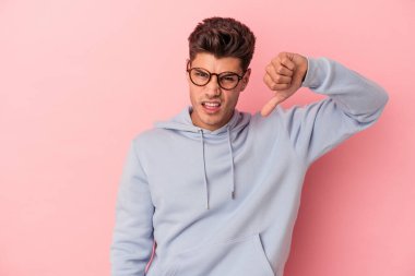 Pembe arka planda izole edilmiş genç beyaz adam baş parmağını aşağı gösteriyor ve hoşlanmadığını ifade ediyor..