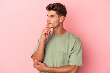 Pembe arka planda izole edilmiş genç beyaz adam şüpheli ve şüpheci bir ifadeyle yana bakıyor..