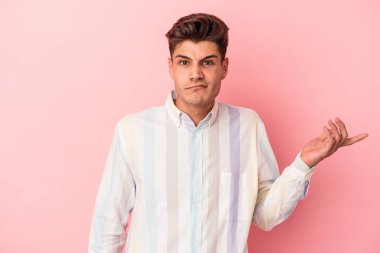 Pembe arka planda soyutlanmış genç beyaz bir adam sorgulama sırasında omuz silkiyor ve şüphe duyuyor..