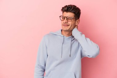 Pembe arka planda izole edilmiş genç beyaz bir adam stresten dolayı boynu ağrıyor, masaj yapıyor ve elle dokunuyor..