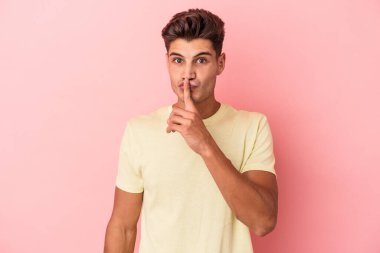 Pembe arka planda izole edilmiş genç beyaz bir adam ya sır saklıyor ya da sessizlik istiyor..