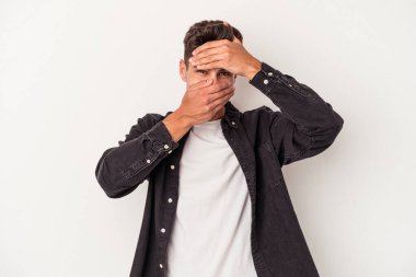 Beyaz arka planda izole edilmiş genç beyaz bir adam kameraya parmaklarıyla göz kırpıyor, yüzünü kapatmaktan utanıyor..