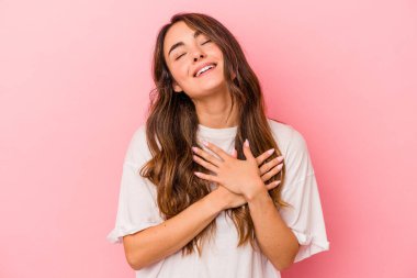 Pembe arka planda izole edilmiş genç beyaz bir kadın, dostane bir ifadeye sahip, avuçlarını göğsüne bastırıyor. Aşk konsepti.