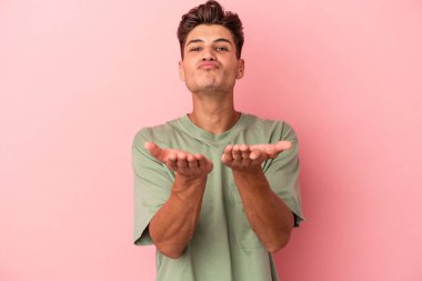 Genç beyaz adam pembe arka planda izole edilmiş dudaklar kıvrılmış ve hava öpücüğü göndermek için avuç içleri tutulmuş..