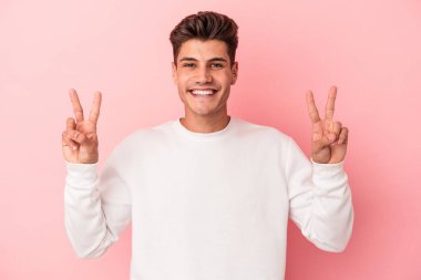 Pembe arka planda izole edilmiş genç beyaz adam zafer işareti gösteriyor ve gülümsüyor..