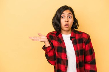 Sarı arka planda izole edilmiş genç Latin kadın, avuç içinde kopya yeri tutmaktan etkilenmiş..