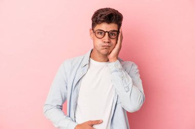 Pembe arka planda izole edilmiş genç beyaz adamın yanakları şişer, yorgun bir ifadesi vardır. Yüz ifadesi kavramı.