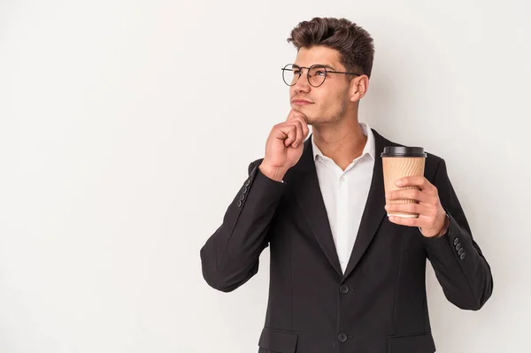 年轻的生意人拿着咖啡 带着怀疑和怀疑的表情 侧视着白色背景的咖啡 — 图库照片