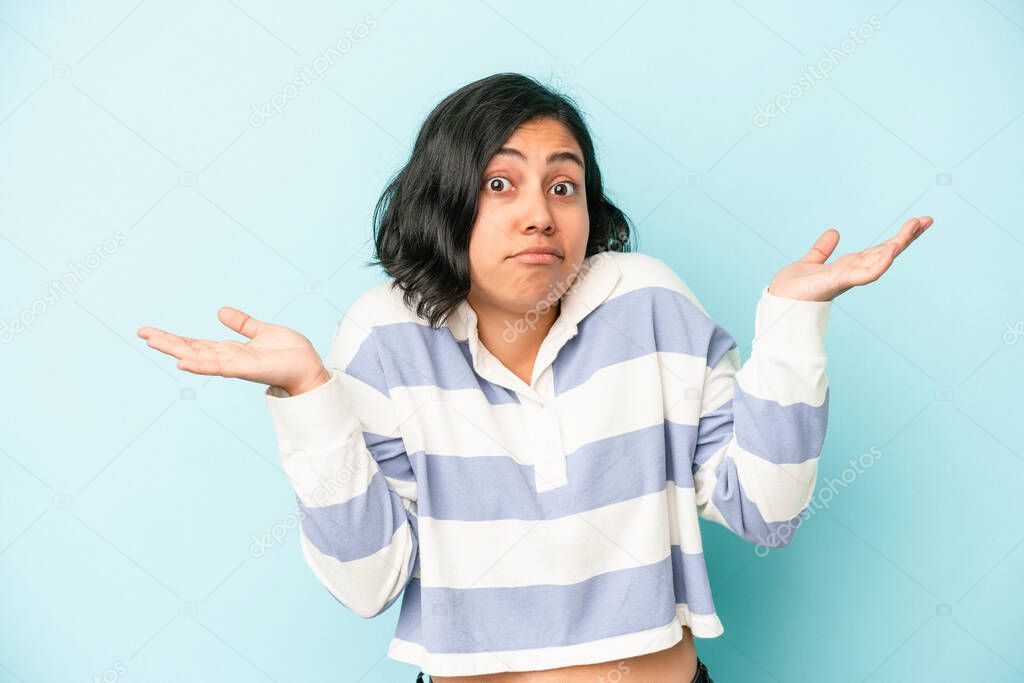Young latin woman isolated on blue background doubting and shrugging shoulders in questioning gesture.
