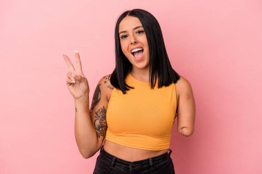 Tek kollu beyaz bir kadın pembe arka planda izole edilmiş neşeli ve kaygısız parmaklarıyla barış sembolü gösteriyor..