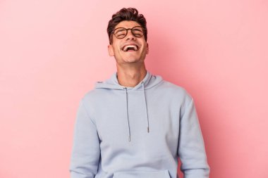 Genç beyaz adam pembe arka planda izole edilmiş rahat ve mutlu bir şekilde gülüyor, boynunda dişlerini gösteriyor..