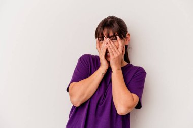 Genç Arjantinli kadın beyaz arka planda izole edilmiş. Kameraya parmaklarıyla göz kırpıyor. Yüzünü kapatmaktan utanıyor..