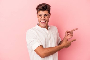Pembe arka planda izole edilmiş genç beyaz adam işaret parmağıyla işaret ederek heyecanlanıyor..