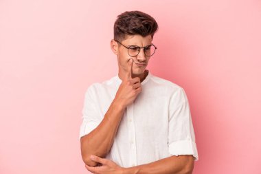 Pembe arka planda izole edilmiş genç beyaz adam şüpheli ve şüpheci bir ifadeyle yana bakıyor..