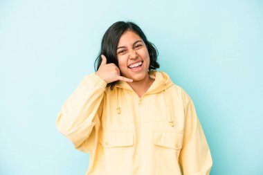 Mavi arka planda izole edilmiş genç Latin kadın parmakları olan bir cep telefonu hareketi gösteriyor..