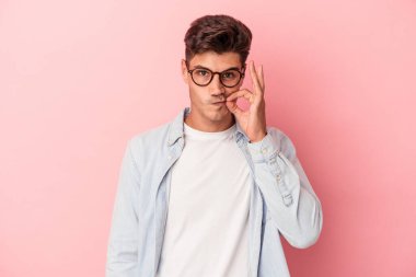 Pembe arka planda izole edilmiş genç beyaz bir adam parmakları dudaklarında bir sır saklıyor..