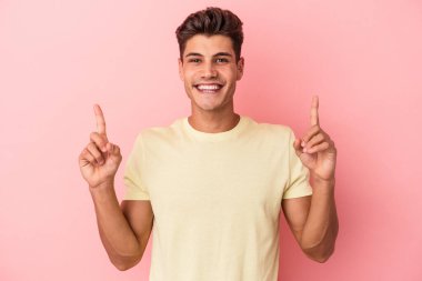 Pembe arka planda izole edilmiş genç beyaz adam iki parmağı da boş bir alan gösteriyor..