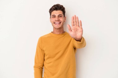 Beyaz arka planda izole edilmiş genç beyaz bir adam gülümseyerek beş numarayı parmaklarıyla gösteriyor..