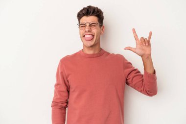 Beyaz arka planda izole edilmiş genç beyaz bir adam parmaklarıyla kaya hareketi gösteriyor.