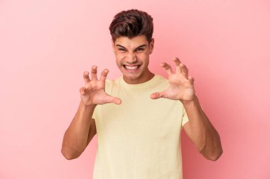 Pembe arka planda izole edilmiş genç beyaz adam pençelerini kedi taklidi yaparken gösteriyor, agresif bir hareket..