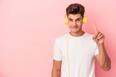 Pembe arka planda müzik dinleyen beyaz bir adam bir numarayı parmağıyla gösteriyor..