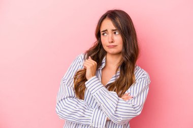 Pembe arka planda izole edilmiş genç beyaz kadın kafası karışmış, kuşkulu ve güvensiz hissediyor..