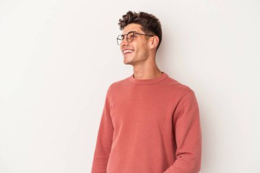 Beyaz arka planda izole edilmiş genç beyaz adam gevşemiş ve mutlu bir şekilde gülüyor, boynunda dişlerini gösteriyor..