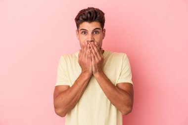 Pembe arka planda izole edilmiş genç beyaz adam şok olmuş, ağzı ellerle kaplanmış, yeni bir şey keşfetmeye hevesli..