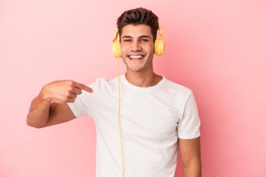 Pembe arka planda izole edilmiş müzik dinleyen beyaz bir adam gömlek fotokopi alanını elle işaret ediyor, gururlu ve kendinden emin.