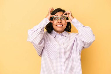 Sarı arka planda izole edilmiş genç Latin bir kadın bir başarı fırsatı bulmak için gözlerini açık tutuyor..