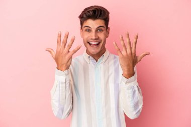 Pembe arka planda izole edilmiş genç beyaz adam on numarayı elleriyle gösteriyor..