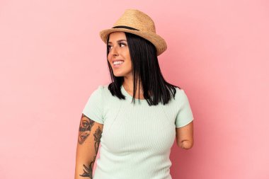 Tek kollu beyaz bir kadın pembe arka planda izole edilmiş yaz şapkası takıyor. Gülümsüyor, neşeli ve keyifli görünüyor..