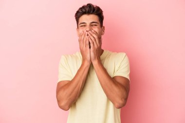Pembe arka planda izole edilmiş genç beyaz bir adam bir şeye gülüyor, elleriyle ağzını kapatıyor..