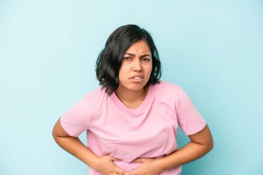 Mavi arka planda karaciğer ağrısı ve karın ağrısı çeken genç bir Latin kadın..