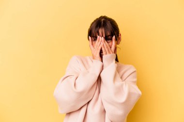 Sarı arka planda izole edilmiş genç Arjantinli kadın kameraya parmaklarıyla göz kırpıyor, yüzünü kapatmaktan utanıyor..