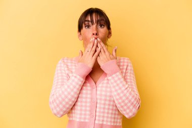 Sarı arka planda izole edilmiş genç Arjantinli kadın şok olmuş, ağzı ellerle kaplanmış, yeni bir şey keşfetmeye hevesli..