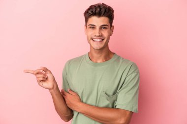 Pembe arka planda izole edilmiş genç beyaz adam işaret parmağıyla işaret ederek gülümsüyor..