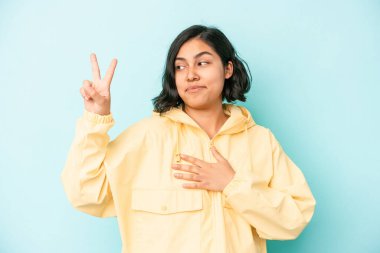 Mavi arka planda izole edilmiş genç Latin bir kadın yemin ediyor, elini göğsüne koyuyor..