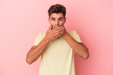 Pembe arka planda izole edilmiş genç beyaz adam elleri endişeli bir şekilde ağzı örtüyor..