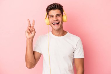 Pembe arka planda izole edilmiş müzik dinleyen beyaz bir adam neşeli ve kaygısız parmakları olan bir barış sembolü gösteriyor..