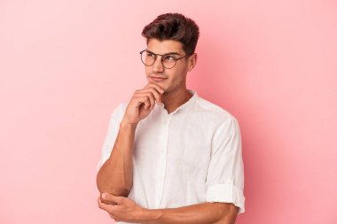 Pembe arka planda izole edilmiş genç beyaz adam rahatlamış bir şeyin fotokopi odasına baktığını düşünüyor..