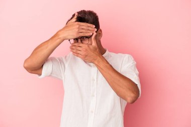 Pembe arka planda izole edilmiş genç beyaz adam kameraya parmaklarıyla göz kırpıyor, yüzünü kapatmaktan utanıyor..