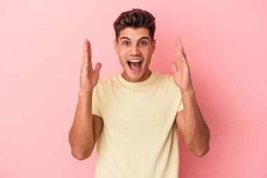 Pembe arka planda izole edilmiş genç beyaz bir adam zaferi ya da başarıyı kutluyor, şaşırıyor ve şok oluyor..