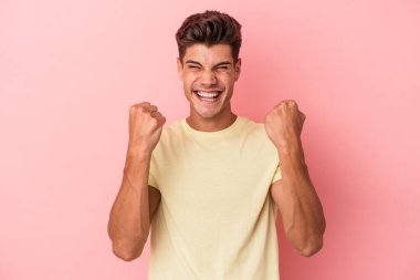 Pembe arka planda soyutlanmış, tasasız ve heyecanlı genç bir beyaz adam. Zafer konsepti.